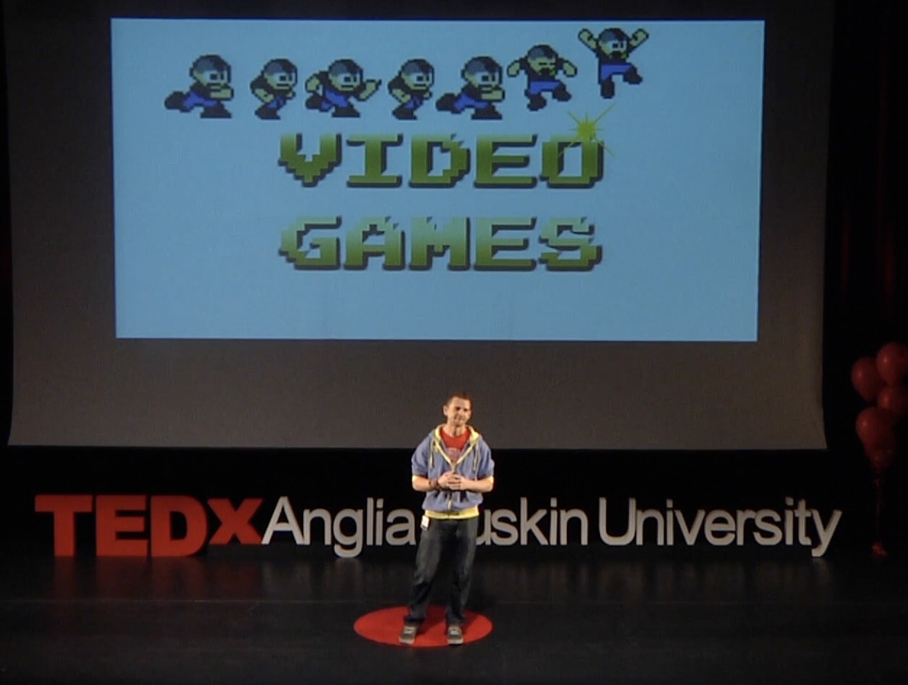 Mark on stage at TEDx Anglia Ruskin University, in front of a slide that says Video Games